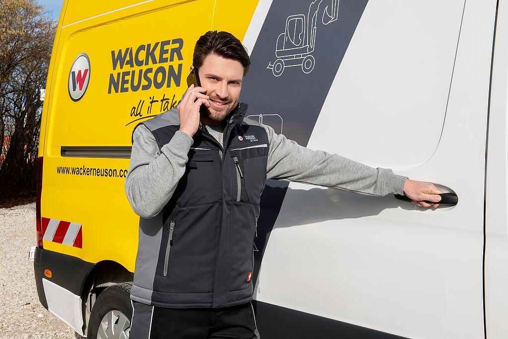 Wacker Neuson employee standing in front of Wacker Neuson service vehicle while on the phone.